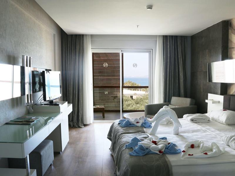 Světle zařízený hotelový pokoj s manželskou postelí a balkonem s výhledem na moře