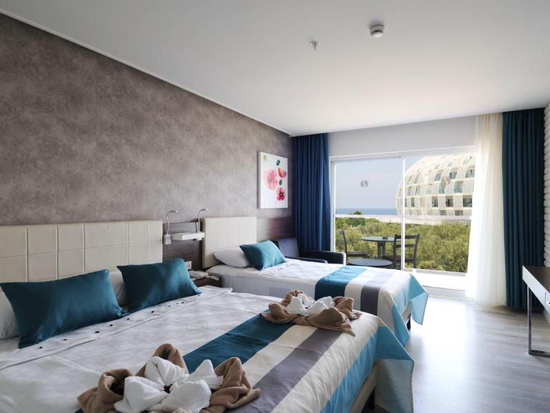 Moderní hotelový pokoj se dvěma postelemi, balkonem a výhledem na zelenou krajinu.