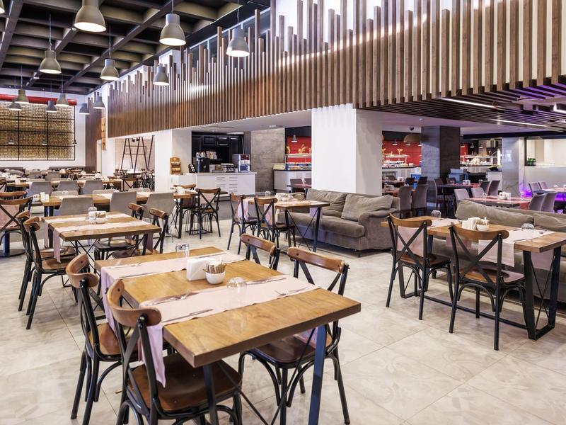 Moderní restaurace s dřevěnými a kovovými židlemi, velkými dřevěnými stoly a stylovým osvětlením.