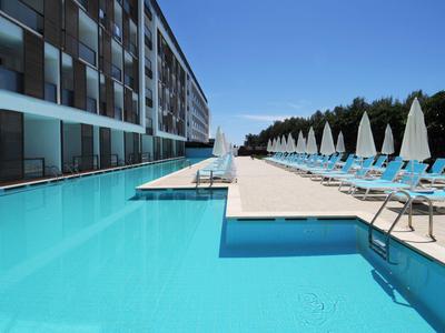 Moderní venkovní bazén s lehátky a slunečníky vedle hotelové budovy za jasné oblohy.