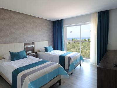 Hotelový pokoj se dvěma postelemi, tyrkysovými akcenty a výhledem na moře skrz velké okno.