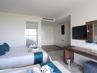 Moderní hotelový pokoj se dvěma jednolůžky, televizí a dřevěným nábytkem.