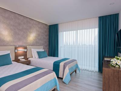 Moderní hotelový pokoj se dvěma jednolůžky, modrými akcenty a oknem se závěsy.