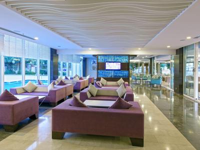 Světlý, moderní hotelový salonek s hnědými pohovkami a velkými okny s výhledem ven.