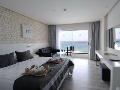 Moderní hotelový pokoj s manželskou postelí, sedačkou, televizí a výhledem na moře přes velká okna