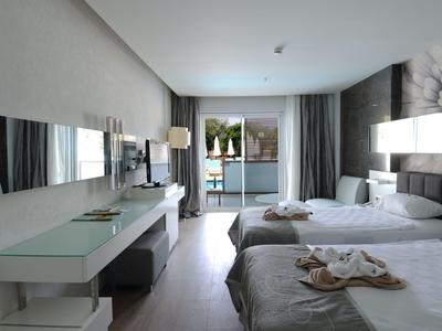 Moderní hotelový pokoj se dvěma postelemi, psacím stolem a balkonem s výhledem na zeleň.