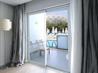 Výhled přes skleněné dveře na terasu s židlemi a venkovní bazén.