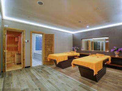 Ruheraum mit zwei Liegen, orangenen Decken, indirekter LED-Beleuchtung und Zugang zu Sauna und Dusche.