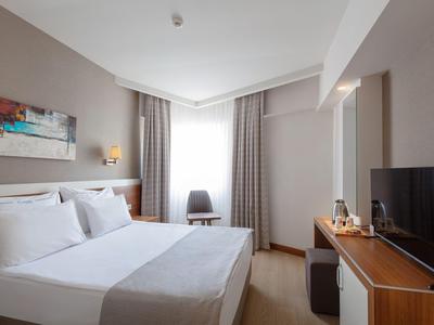 Jasně zařízený hotelový pokoj s velkou postelí, židlí a TV na dřevěné komodě