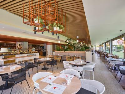 Modern restaurant met witte en zwarte stoelen, houten tafels en grote ramen met uitzicht op het terras.