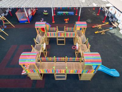 Bunter Holz-Spielplatz mit Türmen, Rutschen und Kletterelementen auf weitem, schwarzem Boden.