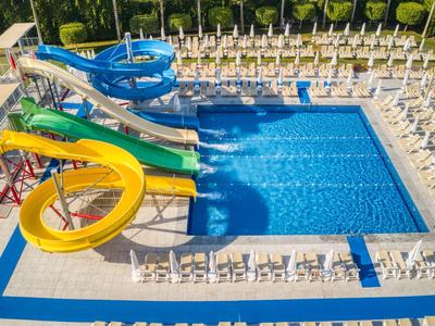 Schwimmbecken mit Rutschen in Gelb, Grün, Blau und Weiß, umgeben von Liegestühlen und Bäumen.