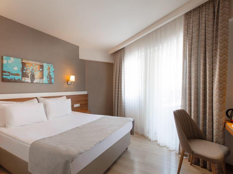 Moderne hotelkamer met groot bed, stoel en bureau voor een raam van vloer tot plafond