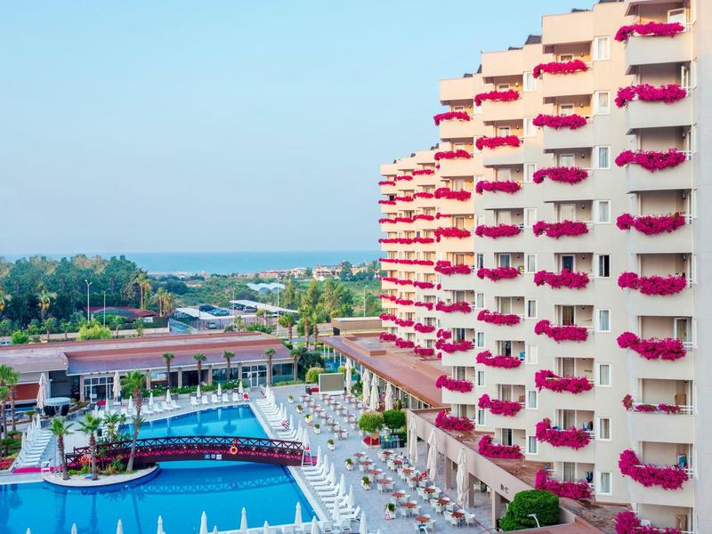 Hotelcomplex met zwembad, witte ligbedden en gebouwen met rode bloemen op balkons.
