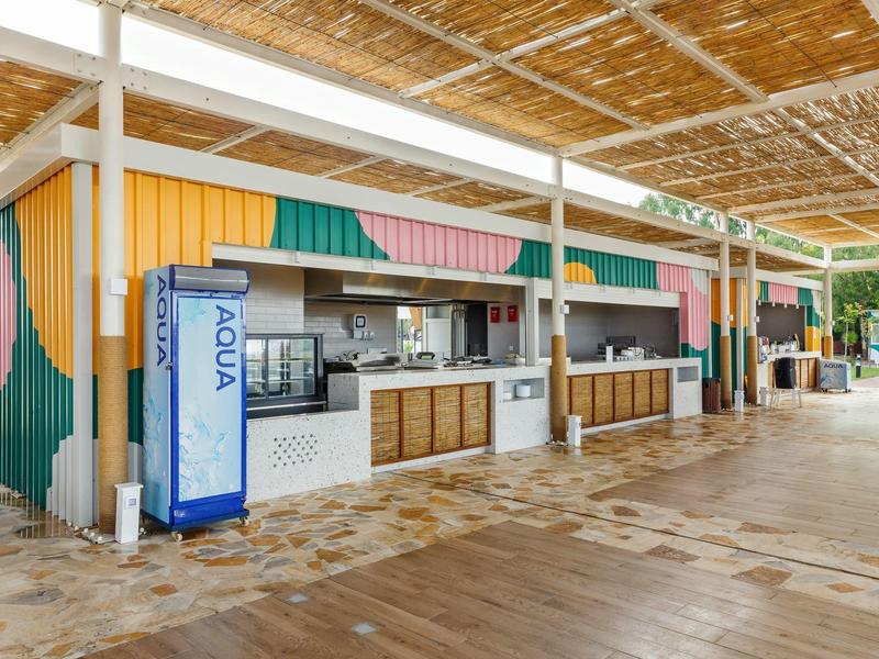 Open bar met houten toonbank en drankautomaat onder een overkapping met houten dakstructuur.