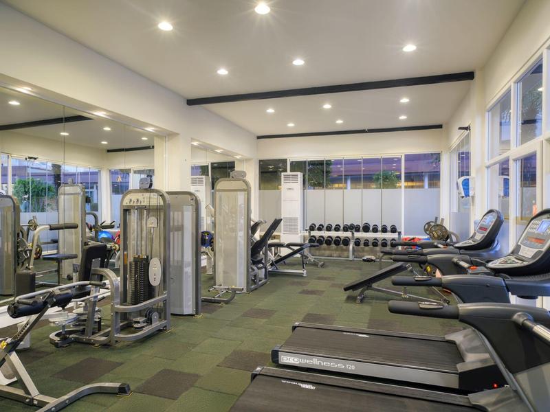 Moderne fitnessruimte met loopbanden, gewichten en grote ramen met uitzicht naar buiten.