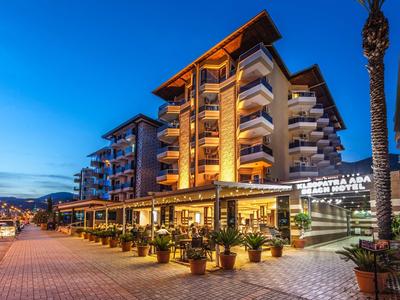 Modernes Hotel mit beleuchteten Balkonen, Außenrestaurant und Palmen bei Abenddämmerung.