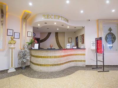 Helle Hotellobby mit geschwungenem Empfangstresen, dekorativen Pflanzen und Beleuchtung.