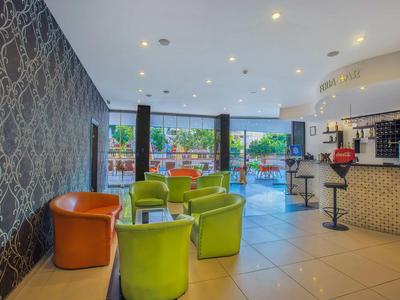 Modernes Café mit grünen Sesseln, orangen Stühlen, großen Fenstern und heller Raumbeleuchtung.