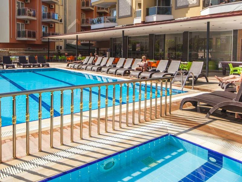 Außenpool mit Liegestühlen, Sonnenschirmen und moderner Wohnanlage im Hintergrund.