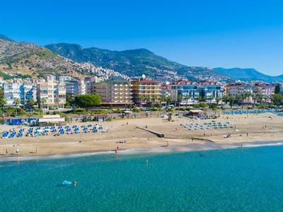 Beach with sun loungers, hotels, and mountains in the background under clear sky