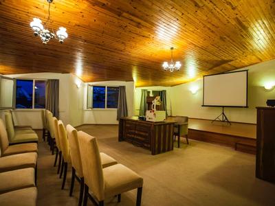 Conference room with rows of chairs, wooden ceiling, and projector screen on the wall.