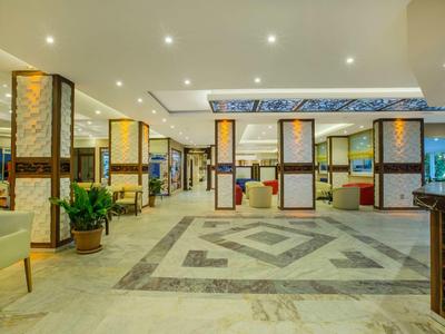 Spacious modern hotel lobby with seating areas, plants, and bright ceiling lights.
