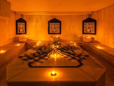 Warm, dimly lit hammam with central water basin, candlelight, and tile decorations on the walls.