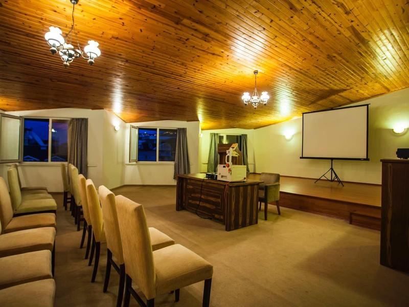 Conference room with rows of chairs, wooden ceiling, and projector screen on the wall.