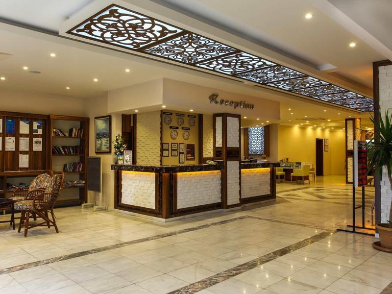 Hotel lobby with reception desk, seating area, and decorative ceiling panels.