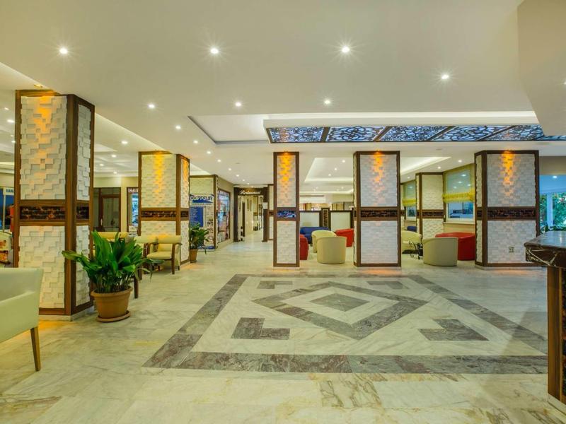 Spacious modern hotel lobby with seating areas, plants, and bright ceiling lights.