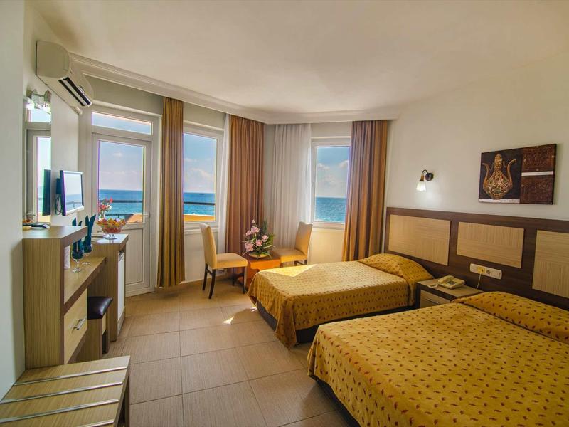 Hotel room with two beds, windows overlooking the sea, and a seating area with chairs and table.