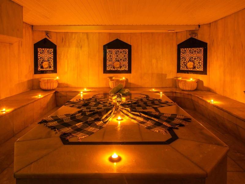 Warm, dimly lit hammam with central water basin, candlelight, and tile decorations on the walls.