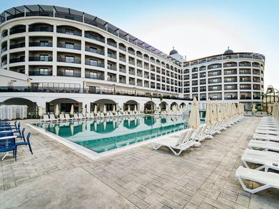 Modernes mehrstöckiges Hotel mit Pool, Sonnenliegen und klaren blauen Himmel im Hintergrund.