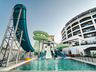 Wasserbahn mit grünen und blauen Rutschen neben einem modernen, weißen Hotelgebäude.