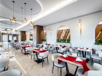 Moderner heller Restaurantraum mit weißen Wänden, Stühlen und roten Tischläufern, elegante Beleuchtung.