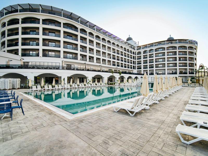 Velký hotel s venkovním bazénem a mnoha bílými lehátky na terase.