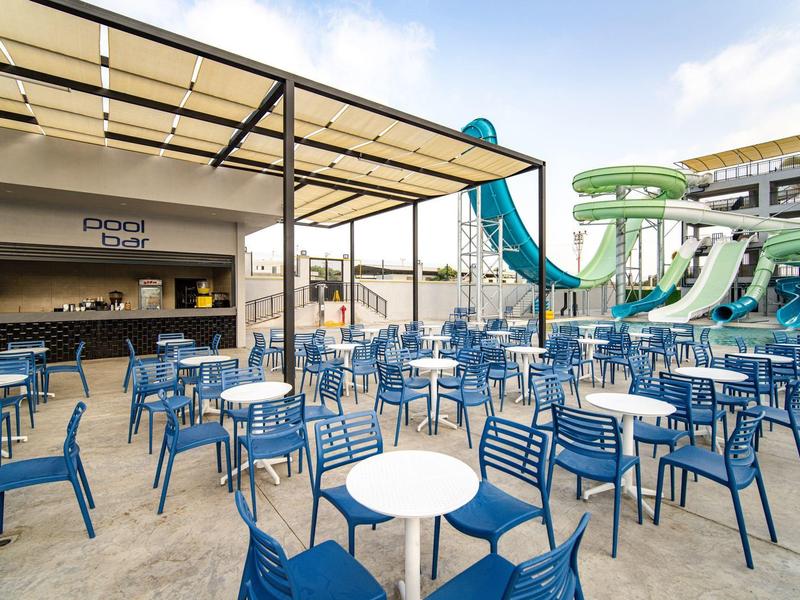Venkovní prostor s modrými židlemi a stoly poblíž vodních skluzavek ve vodním parku.