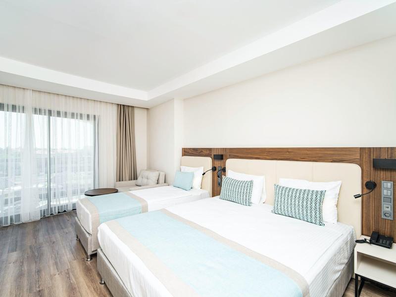 Moderní hotelový pokoj se dvěma velkými postelemi, dřevěným nábytkem a světlými závěsy.