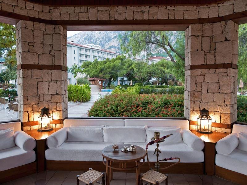 Cozy outdoor lounge with white sofas and stone walls overlooking greenery and mountains.