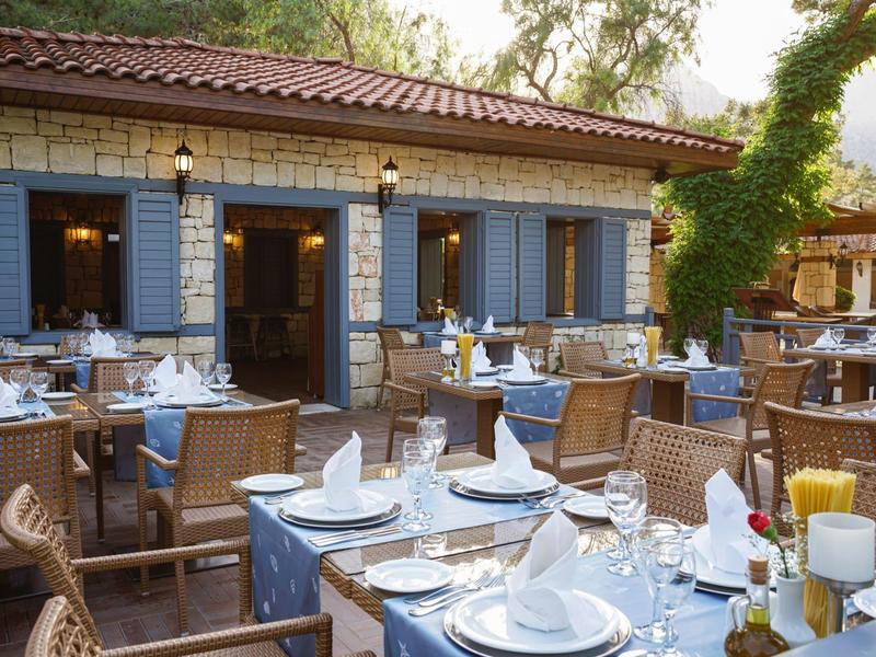 Outdoor restaurant seating with neatly set tables and wooden chairs under a tiled roof.