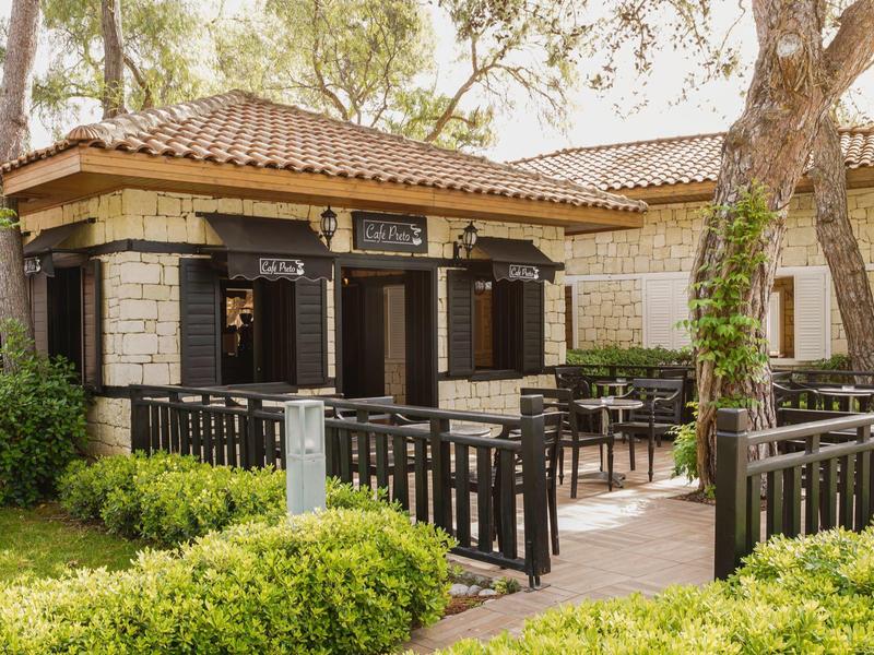 Outdoor seating area with black chairs and tables by a beige building with tiled roof.