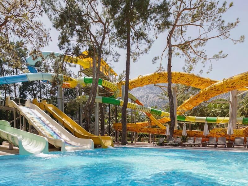 Water park area with multiple water slides and a pool surrounded by trees and lounge chairs.