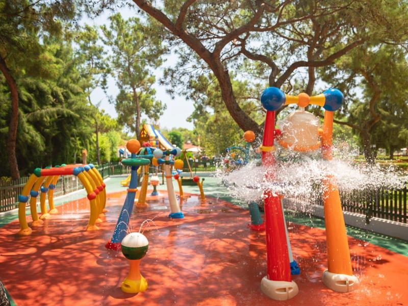Colorful water playground with sprays, slides, and climbing structures under trees.