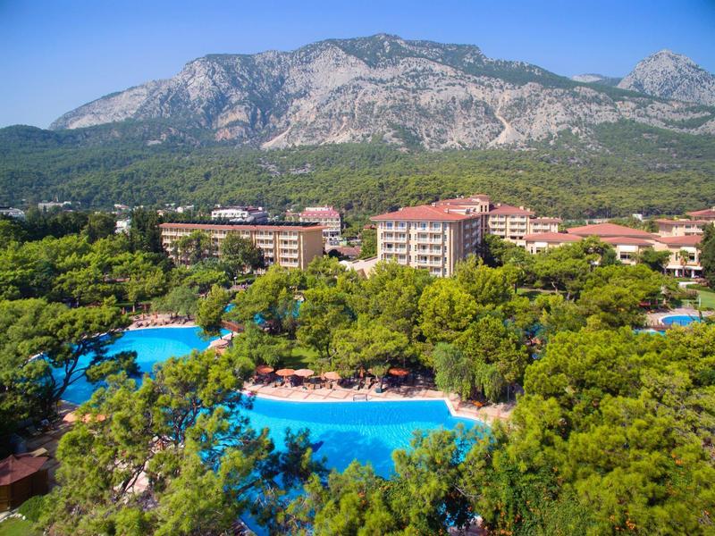 Resort with large blue pools surrounded by green trees and mountains in the background.