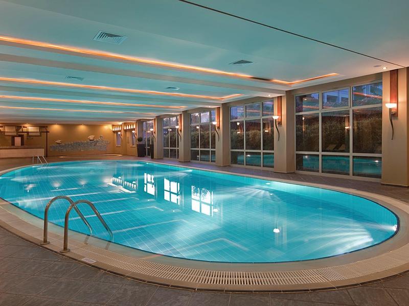 Indoor hotel pool with blue water and large windows showcasing outside view.
