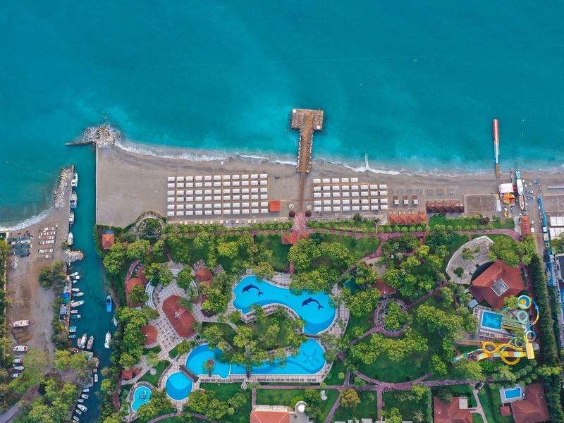 Aerial view of a beach resort with pools, greenery, docks, and rows of beach umbrellas by the sea.