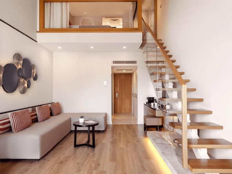 Modern deluxe duplex room with sofa, floating stairs, and wooden flooring.
