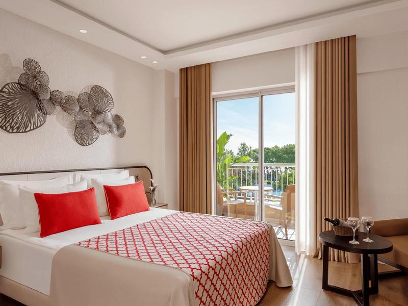 Deluxe family room with king-size bed, red accents, wall art, and balcony overlooking greenery.