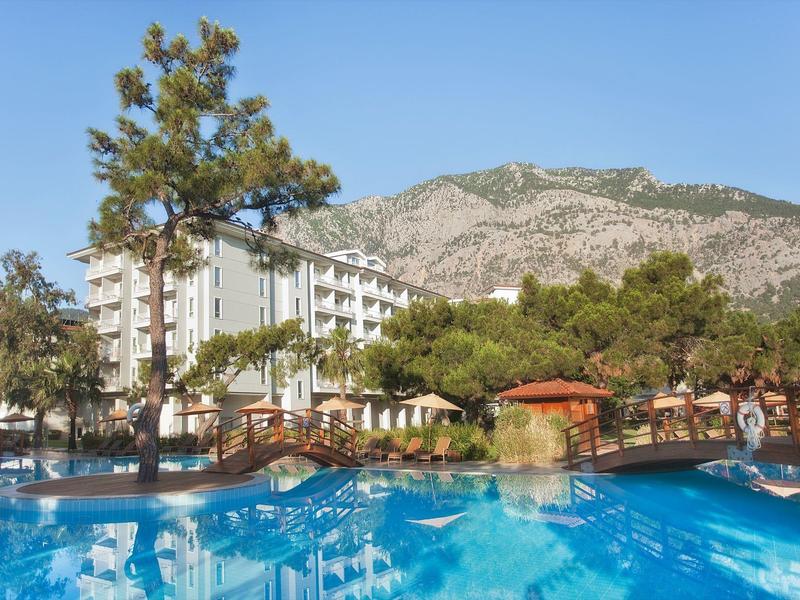 Resort hotel with a large swimming pool, surrounded by trees and mountains in the background.